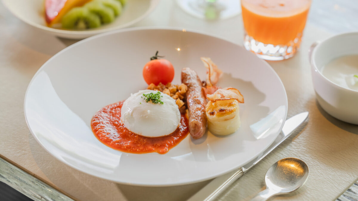 ポーチドエッグを中心に、ソーセージ、ベーコン、トマト、グラタン風ポテトなどが美しく盛り付けられた朝食プレート。