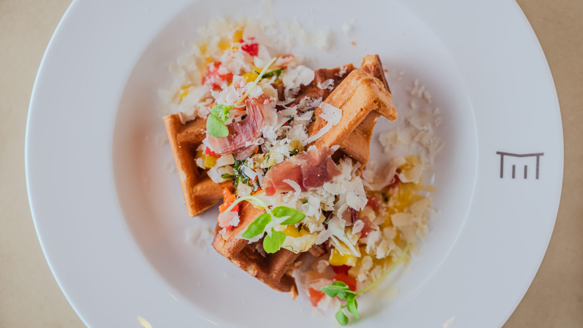 チーズと焼き野菜をトッピングしたセイボリーワッフルが白いプレートに美しく盛り付けられている。