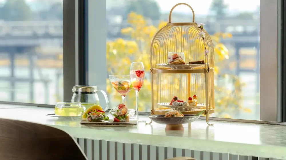 窓辺に並ぶアフタヌーンティーセットとスイーツ、ティーのテーブルセッティング